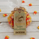 Bag of candy corn with a personalized Halloween tag on a wooden surface.